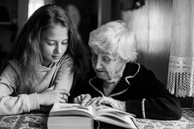 Küçük bir kızla kitap okuyan yaşlı bir kadın. Siyah beyaz fotoğraf.