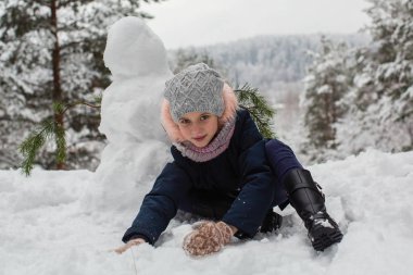 Little girl sculpts snowman in winter snowy Park. clipart