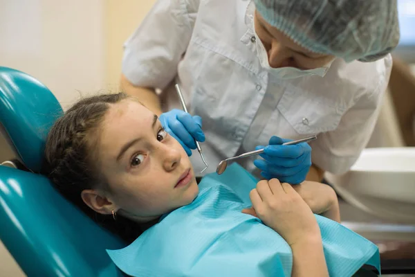 歯医者をしている女歯科医は診療所を訪れる歯医者の椅子に座って悲しい顔をしている少女の歯の検査をする ヘルスケアと生活習慣医学の概念 — ストック写真