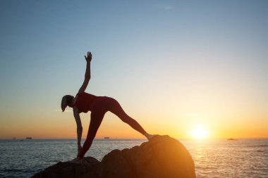 Deniz kıyısında gün batımında yoga egzersizleri yapan bir kadın silueti..