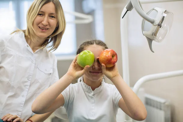 Dentist woman gives apple for smiling teenage girl in dental clinic.
