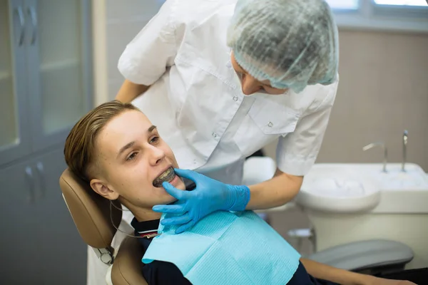 歯医者は男性患者に口腔ガード 取り外し可能な歯列矯正器具及び矯正器具 を歯科事務所に置く — ストック写真