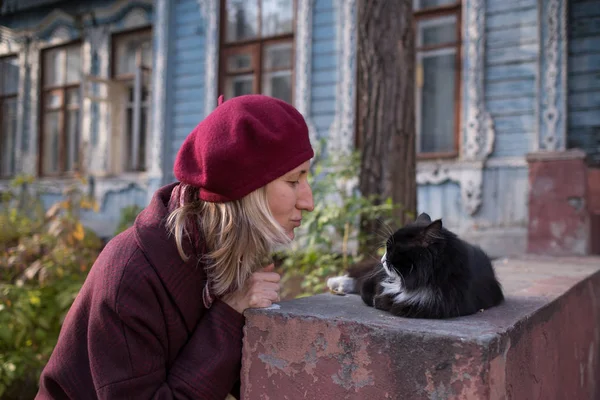 コートとベレー帽の女性はカントリーハウスのポーチで猫と遊ぶ — ストック写真