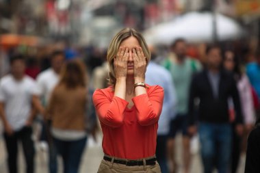 Woman covers his eyes during panic attack in public place.   clipart
