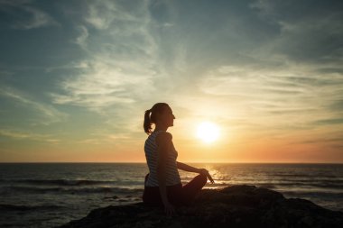 Siluet kadın gün batımında deniz sahilinde yoga yapıyor.