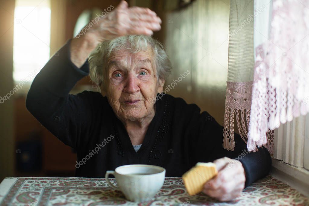 Elderly old woman drinking tea with cookies at home. 