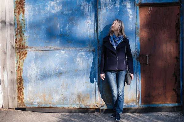 一个金发女人站在铁蓝色的街道墙边 — 图库照片