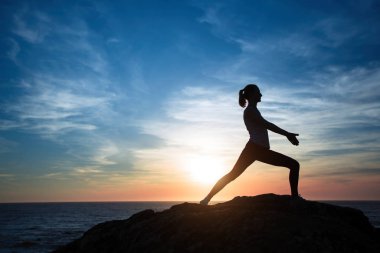 Gün batımında deniz sahilinde egzersiz yapan genç bir kadının silueti.. 