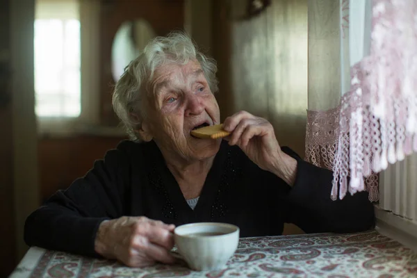 家でクッキーを持ってお茶を飲むお年寄りの女性 — ストック写真