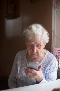 Yaşlı bir kadın emekli evinde elinde akıllı bir telefonla oturuyor..
