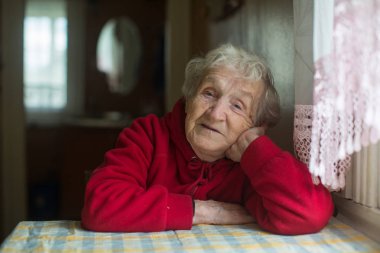 Evde bir masada oturan yaşlı bir kadının portresi..