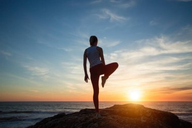 Fetness woman silhouette performs concentration exercises during amazing sunset on the sea coast.