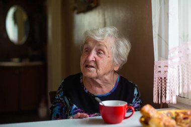 Evinin mutfağındaki yaşlı kadın masada oturuyor..