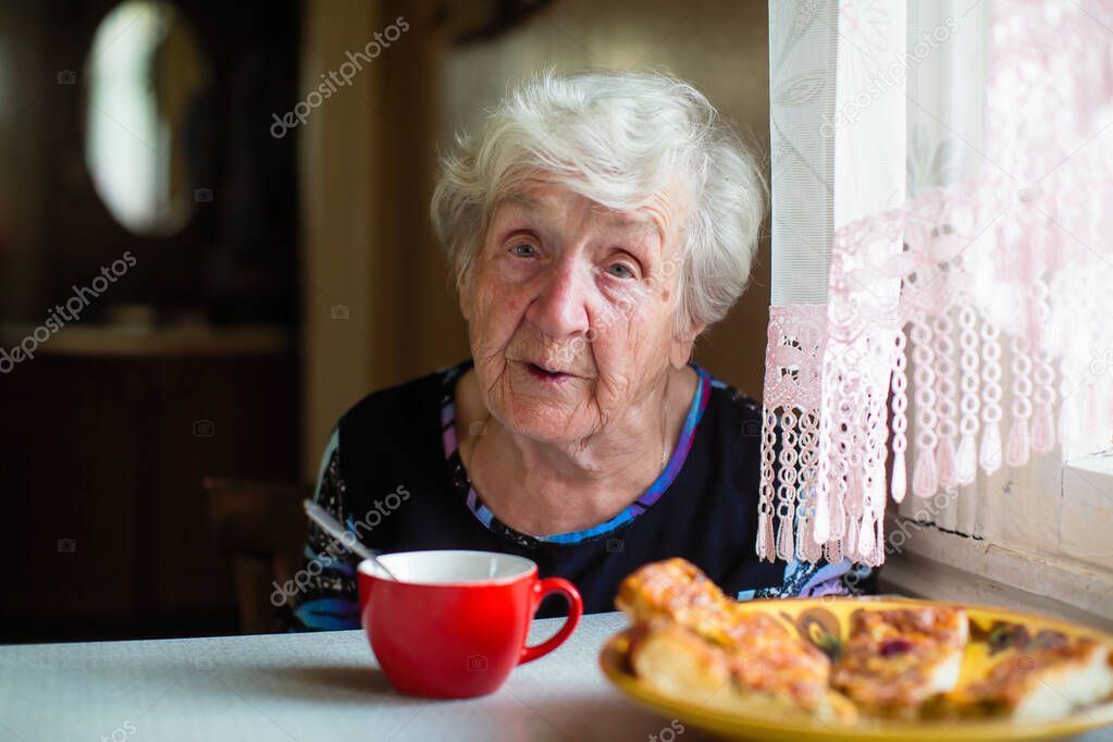 An elderly old woman has breakfast sitting at her home.