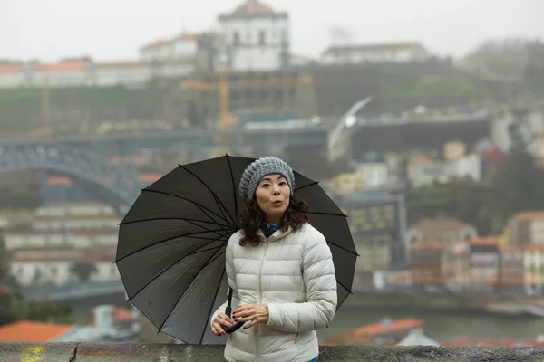 Asian woman with an umbrella in cloudy weather - Dom Luis I Bridge in Porto, Portugal.