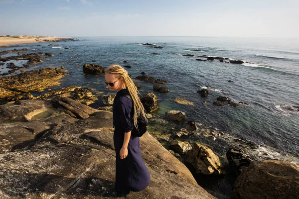岩の多い海の岸に長い光のドレッドロックを持つ女性が立っている — ストック写真