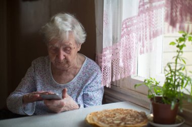 Yaşlı bir kadın elinde akıllı bir telefonla oturuyor..