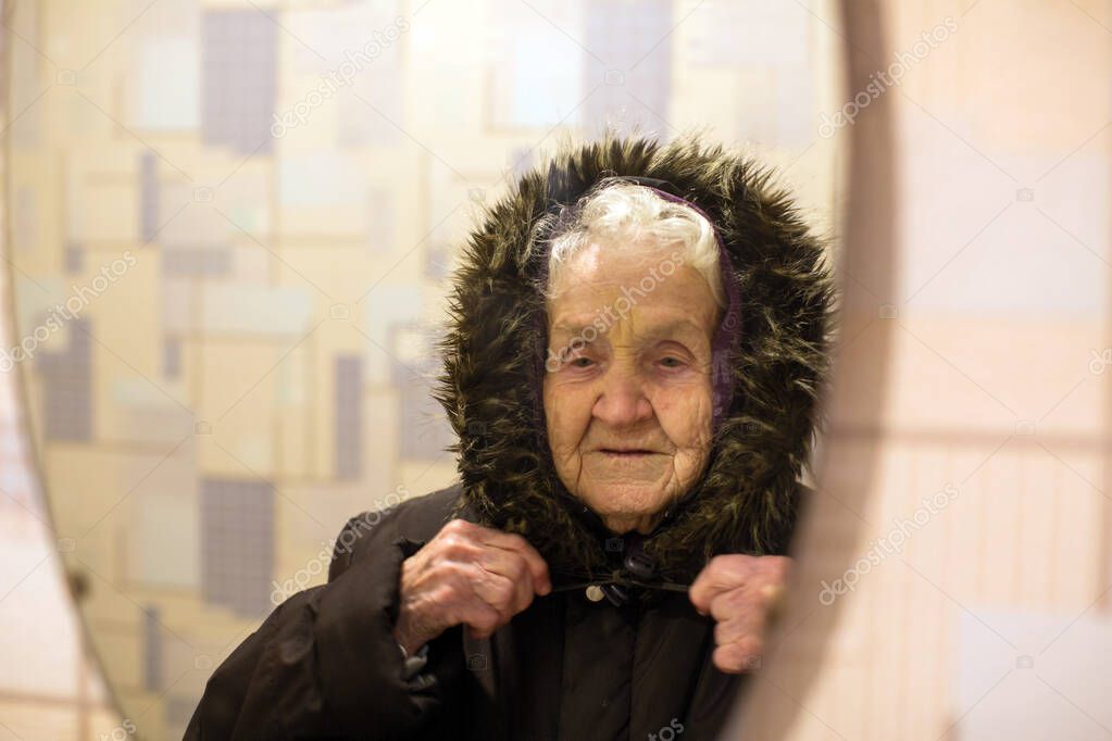 An elderly woman reflection in the mirror wearing winter outerwear.