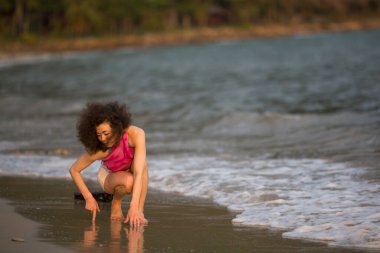 Çok kültürlü Asyalı kadın deniz kıyısındaki sörf hattında diz çöker.. 