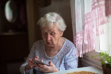 Çok yaşlı bir kadın evde akıllı telefon kullanıyor..