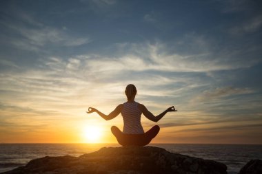 Yoga yapan kadın gün batımında denizde meditasyon yapıyor..