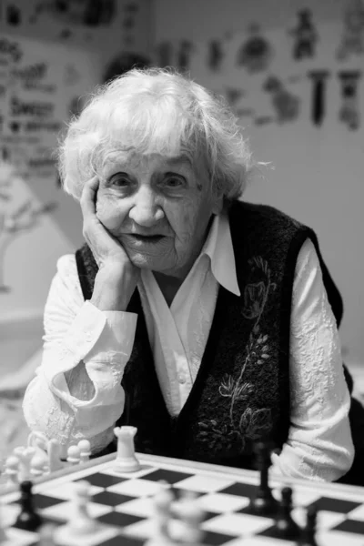 An old woman is playing chess. Black and white photo portrait.