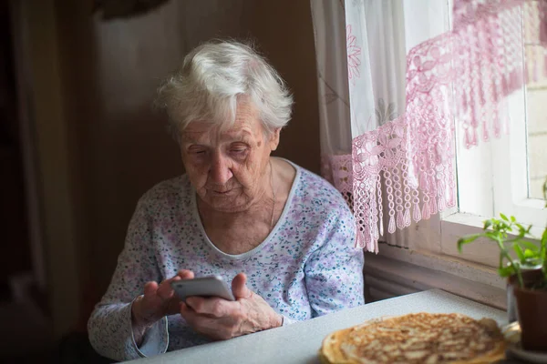一位老妇人手里拿着智能手机坐在那里 — 图库照片