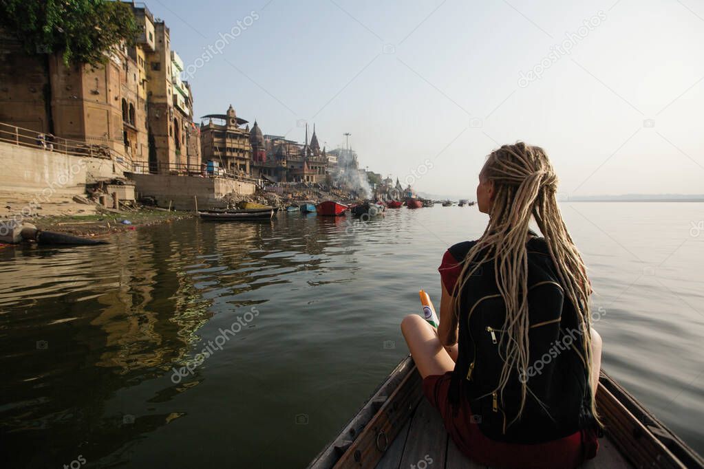 Travel woman on a boat glides on Ganges river along the shore of Varanasi, India.