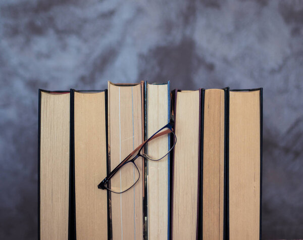 Set of books ordered with glasses on them that symbolize their regular reading. Image on an abstract background