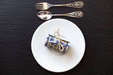 100 dolarlık banknotları küçük çatal ve kaşıkla beyaz tabakta yuvarla.