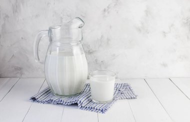 Bir sürahi süt ve bir bardak süt gri arka planda açık tahta bir masada. Sağlıklı doğal ürünler kavramı.