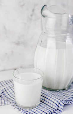 Bir sürahi süt ve bir bardak süt gri arka planda açık tahta bir masada. Sağlıklı doğal ürünler kavramı.
