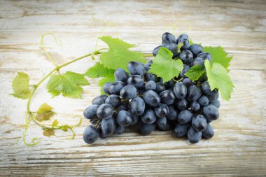 Eski ahşap arka planda yeşil yapraklı bir demet üzüm, yatay olarak, uzayın bir kopyası.