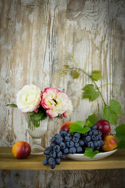 Vintage still Life with roses, grapes and peaches on an old wooden background. Vertically, copy space