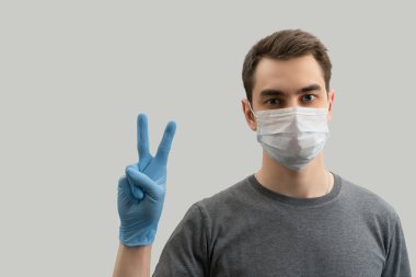 Maske takan genç Avrupalı adam Corona virüsüne karşı barışı gösterdi. Beyaz arka plan Corona virüsünü önlemek için cerrahi maske takan 19 kişi.