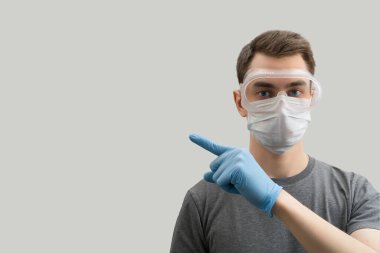 Maske takan ve koruma gözlüğü takan genç Avrupalı adam Corona virüsüne karşı ipucu gösteriyor. Virüs beyaz arka plan Corona virüsü salgınını önlemek için cerrahi maske takan 19 kişi.