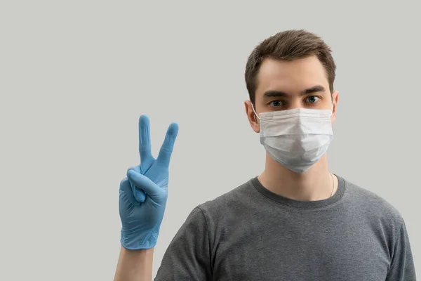 マスクを着用し コロナウイルスに対して平和を示す若いヨーロッパの男は ウイルス白 灰色の背景から防ぐために外科マスクを着用19人をCovidコロナウイルスパンデミック — ストック写真