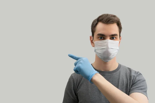 コロナウイルスに対して先端を示すマスクを身に着けている若いヨーロッパの男は ウイルス白 灰色の背景から防ぐために外科マスクを身に着けている19の男コロナウイルスパンデミック — ストック写真