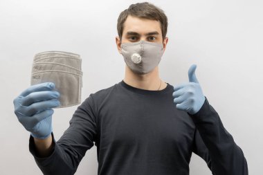 Corona virüsüne karşı maske takan genç Avrupalı bir adam ve virüsün beyaz arka plan Corona virüsünü önlemesi için tekrar kullanılabilir ameliyat maskesi takan 19 kişiyi başparmağında oynatıyor. 