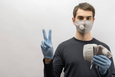 Corona virüsüne karşı maske takan genç Avrupalı bir adam ve virüsün beyaz arka plan Corona virüsünü önlemesi için tekrar kullanılabilir ameliyat maskesi takan 19 kişiyi başparmağında oynatıyor. 