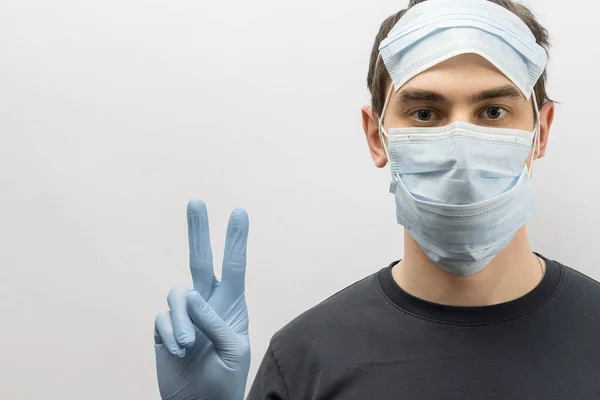 Young european man wearing mask against the corona virus and thumbs up covid 19 man wearing reusable surgical mask to prevent from virus white\grey background Corona virus pandemic funny fun