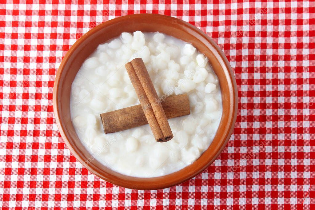 White corn cooked with milk known as canjica, canjicao or mungunza, typical dish of Brazilian gastronomy, in a rustic bowl, on wooden table