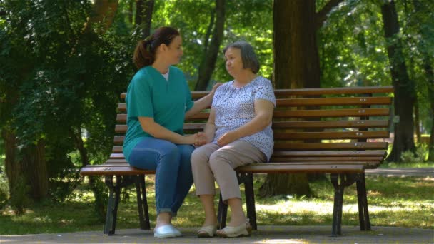 Молодая медсестра проводит солнечный день с пожилой женщиной в парке — стоковое видео