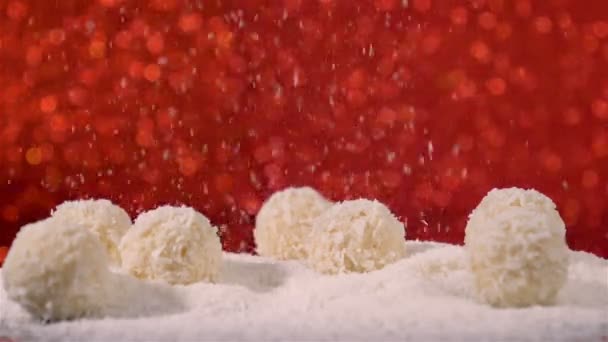 Coconut flakes falling on coconut snowballs white truffles on red glittering background — Stock Video