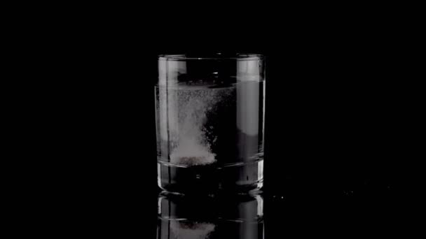 Сияющая таблетка, падающая в стакан воды — стоковое видео