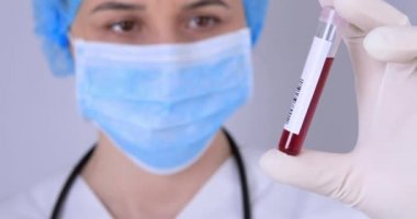 Koruyucu eldivenleri olan kadın doktor kan örneklerini tutuyor ve test ediyor. Virüs testi ve araştırma konsepti. Odaklanma, kan test tüpünden doktora geçmektir. 4k
