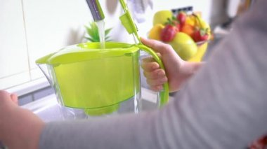 Mutfakta su filtresi dolduran bir kadın var. Musluk suyunun arındırılması ve yumuşatılması. Yakın çekim yavaş çekim