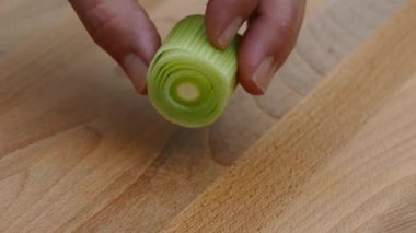 Bahçe pırasasını kesme tahtasının üzerinde bir mutfak bıçağıyla yakın plan 4K ile kesiyor.