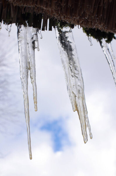 Spring icicles on the roof against cloudy sky