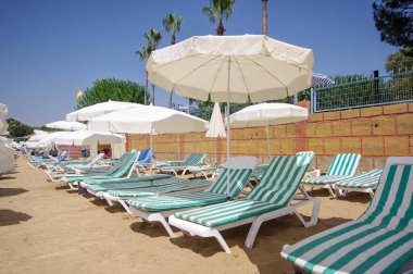 Türkiye 'nin Alanya kentindeki güneşli sahilde plaj şemsiyeleri ve plaj şezlongları